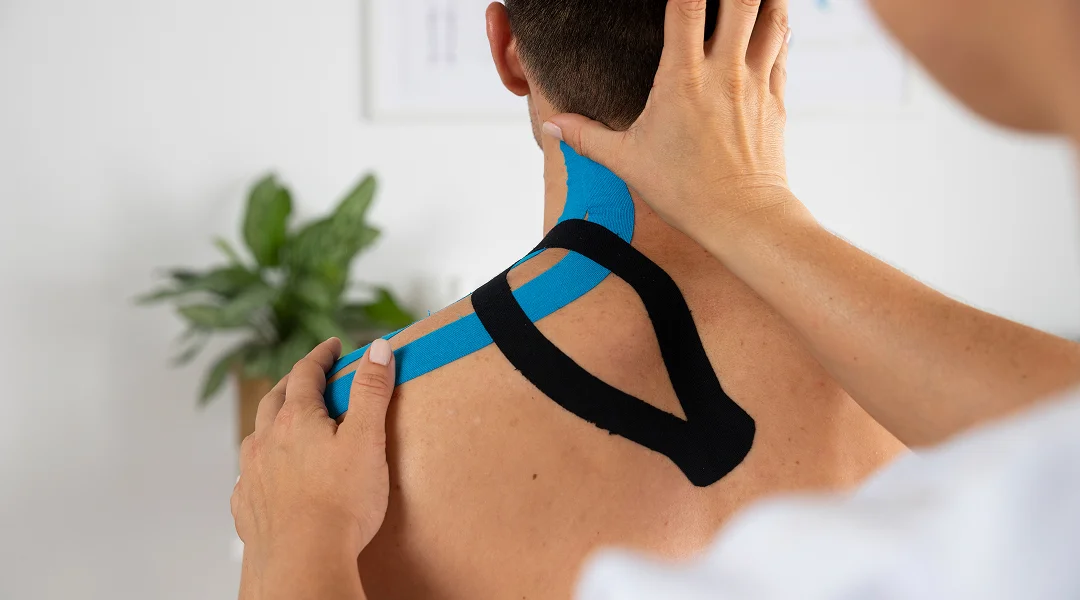 A man receives a back massage while sports taping is applied to his shoulder for support and recovery.