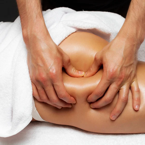 A person receiving a back massage, lying face down on a massage table with a therapist's hands applying pressure.