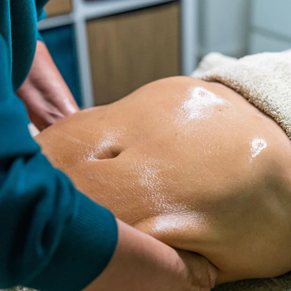 A woman lies on a massage table, receiving a stomach massage from a therapist.
